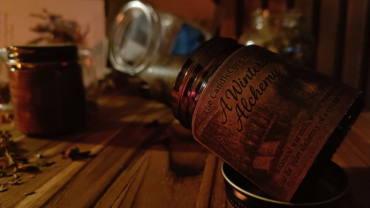 A Winter's Alchemy soy candle resting in soft firelight on a rustic wooden table, creating a warm and intimate winter mood.