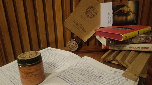 The Storyteller's Cottage soy candle placed on an open journal beside books on a wooden desk, creating a calm reading and writing atmosphere.